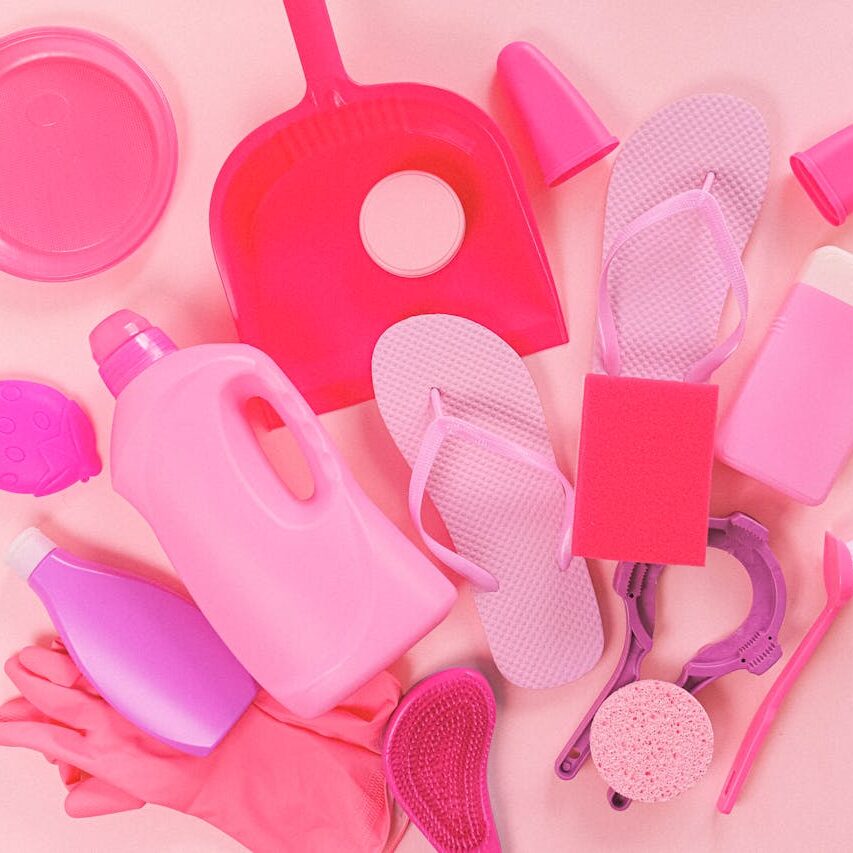 Collection of various plastic detergent bottles and cleaning tools placed on pink background near flip flops and rubber gloves